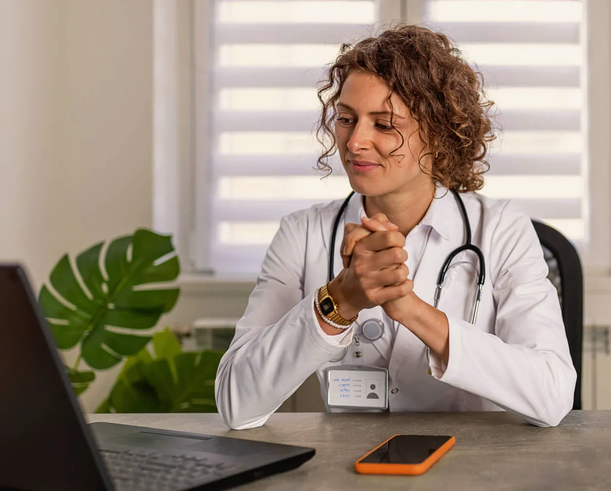 A female doctor working in front of a laptop and mobile phone