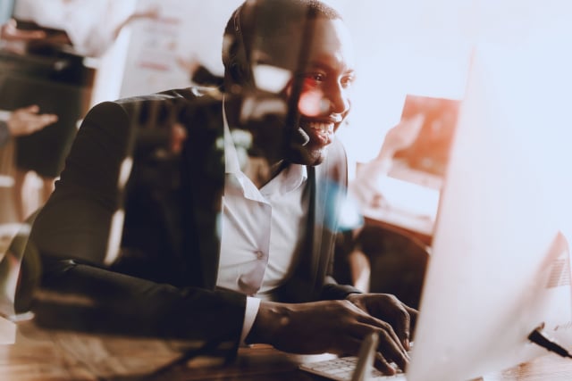 Man sitting at a desk working in a contact centre, wearing headphones and working at his computer.