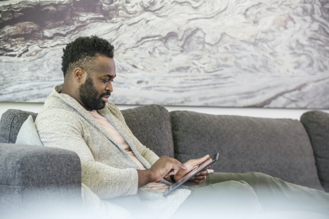 man on a grey sofa is interacting with a digital tablet while working from home