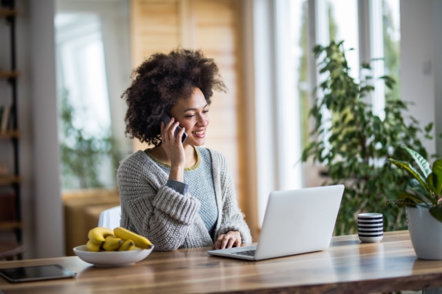 Happy black woman talking on cell phone while reading an e-mail on her laptop.-391