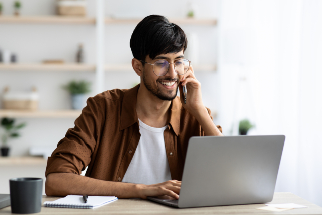 Cheerful indian guy businessman with laptop having phone conversation-406