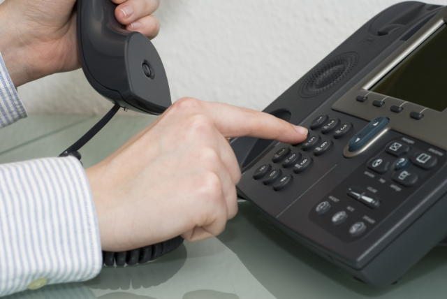 A hand dialing a number on a VoIP phone with AI elements in the background.