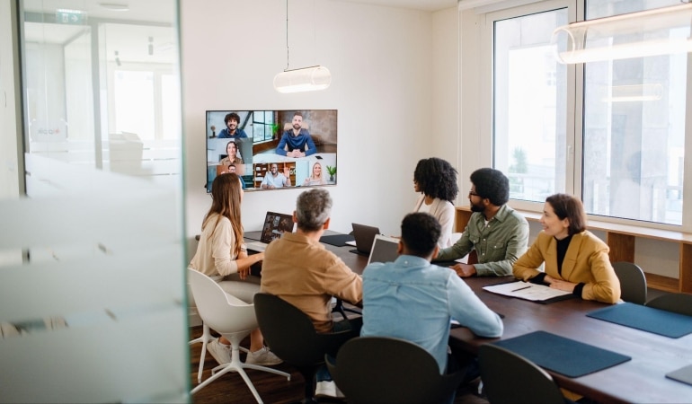 team meeting at conference table with large screen and virtual participant highlighting virtual meeting rooms.