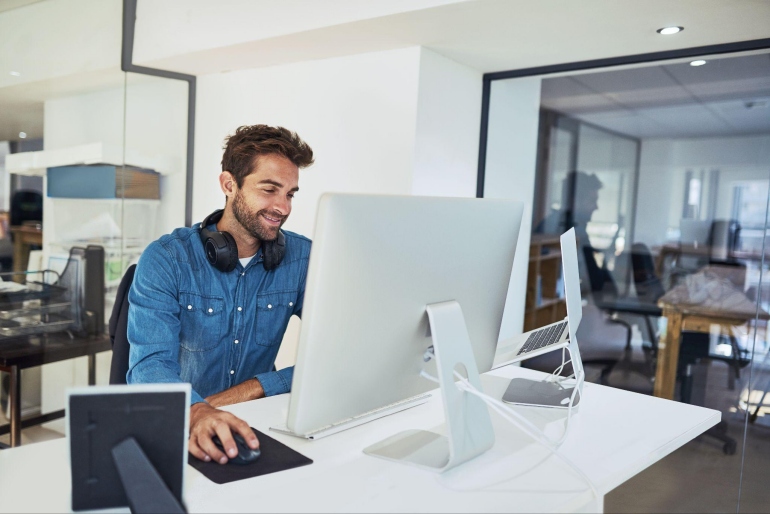 Smiling professional using a desktop computer for cloud communications security tasks in an office